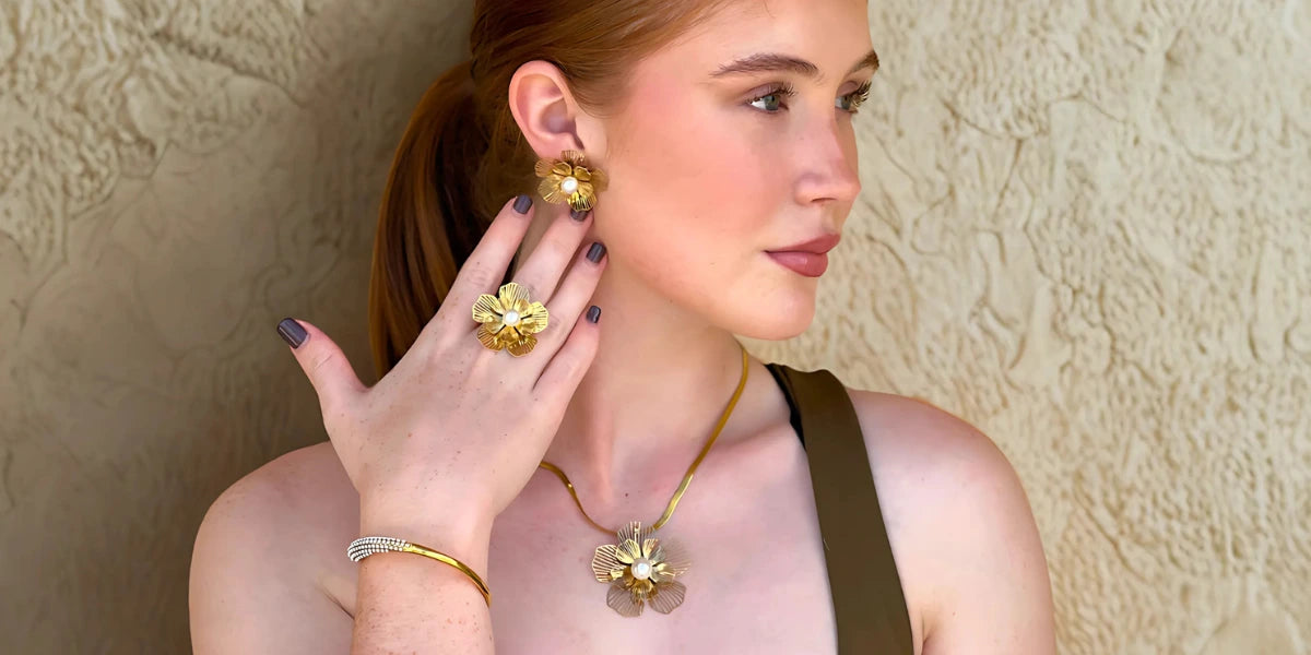 Elegant woman showcasing Reyna Jewellery’s floral 18k gold plated set, featuring statement earrings, ring, bracelet, and necklace 